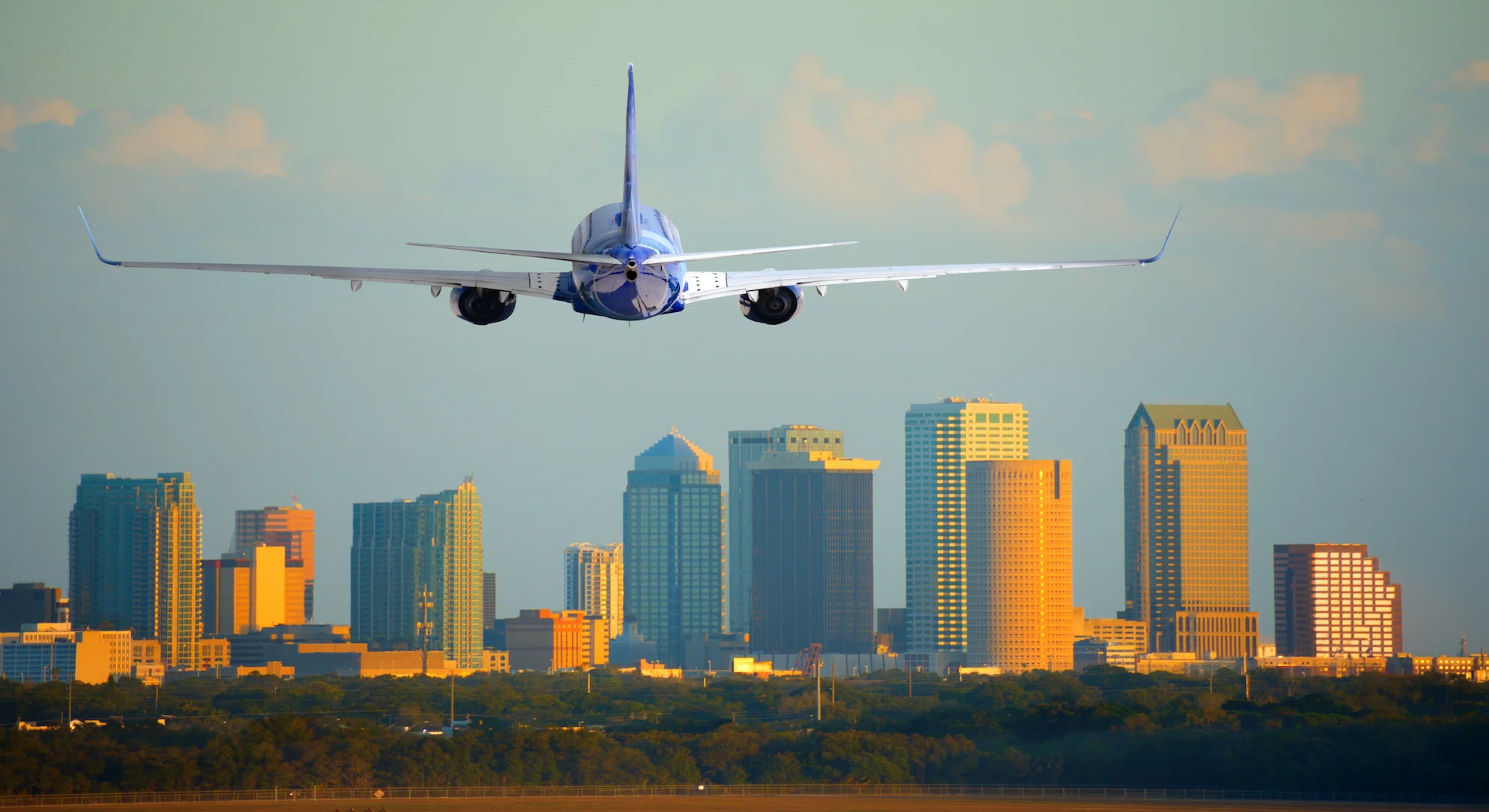A passenger airplane arriving over the downtown Tampa skyline, representing the start of a Florida holiday for UK travellers landing at Tampa International Airport (TPA).