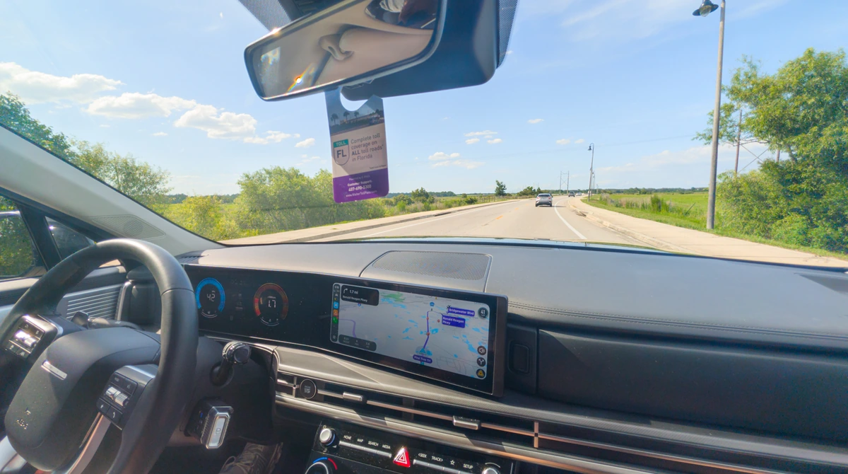 Modern rental car dashboard with GPS navigation system on a straight Florida highway with clear blue sky and vegetation on both sides