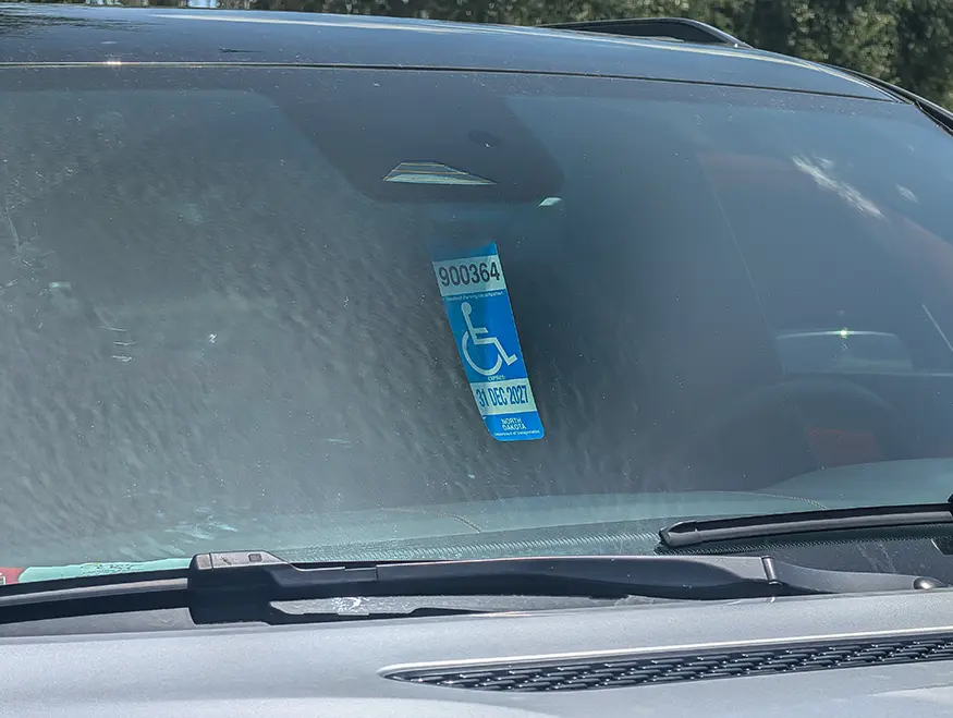 US Disabled Parking Placard Hanging from Vehicle Mirror Florida disabled parking placard hanging from interior rear-view mirror showing wheelchair symbol, illustrating difference from UK Blue Badge dashboard display